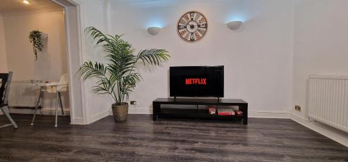 a living room with a tv and a clock on the wall at Spacious & comfy Home- very close to NEC Birmingham ,HS2 & Airport- Perfect for contractors & groups- free parking & Fast WiFi in Marston Green