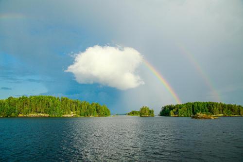 a rainbow in the sky over a lake with trees at Saimaa Experience in Savonlinna