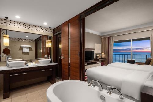 RIHGA Royal Laguna Guam Resort في تامونِنغ: حمام به سرير ومغسلتين وحوض استحمام