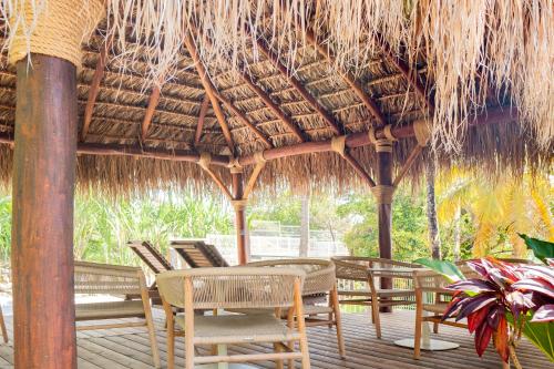 a patio with chairs and a table and a straw roof at Hôtel Iloma in Sainte-Luce