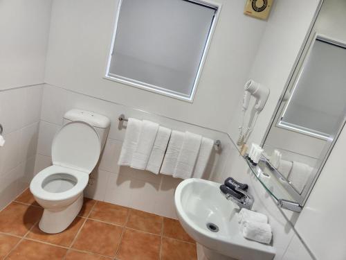a white bathroom with a toilet and a sink at Botany Palms Motel in Auckland