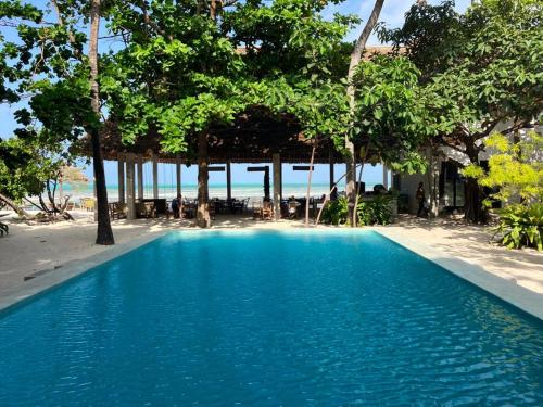 a blue swimming pool next to a beach with trees at Garden Beach Bungalows Jambiani in Jambiani
