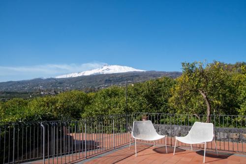 two white chairs sitting on a balcony with a snow covered mountain at Feudogrande Bio Relais Hotel in Fiumefreddo di Sicilia