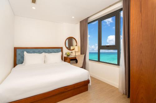 a bedroom with a bed and a window with the ocean at Paris Deli Danang Beach Hotel in Danang