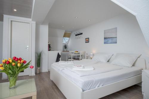 a white bedroom with a white bed and a vase of flowers at Deichhus Nordseeliebe direkt am Deich - Nordsee - Dagebüll - Am Vogelreservat in Dagebüll