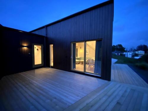 un edificio con terraza de madera y ventana grande en Fresh hytte ved Borestranden med to soverom og hems en Klepp