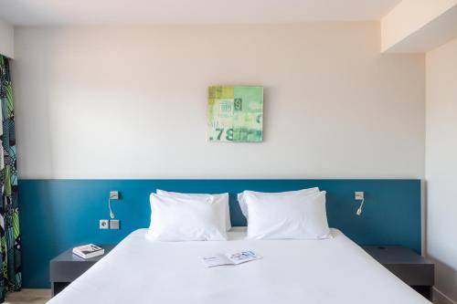 a bedroom with a white bed with a blue wall at Hôtel Serge Blanco - Relais Thalasso & Spa in Hendaye