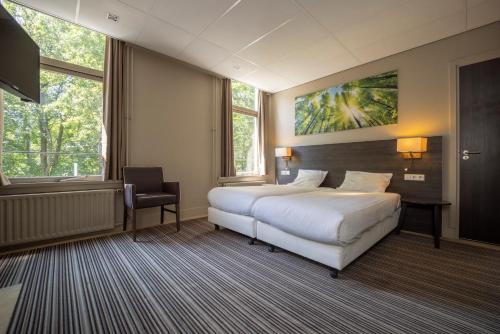 a hotel room with a bed and a desk and two windows at Fletcher Hotel Restaurant Boschoord in Oisterwijk