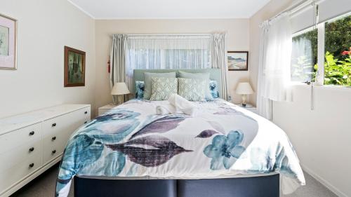 a bedroom with a bed with a blue and white comforter at Little Manly Cottage - Manly Holiday Home in Whangaparaoa