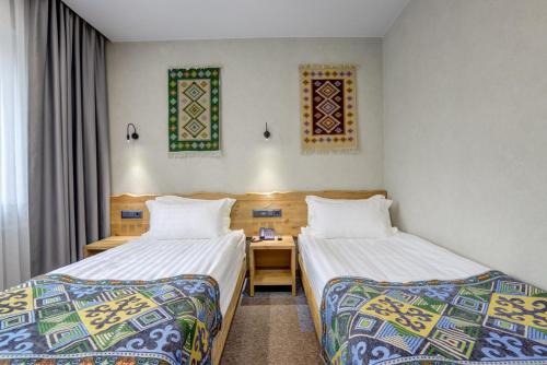 a room with two beds and a desk and windows at My Hotel Bishkek in Bishkek