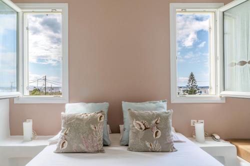een bed met 2 kussens in een kamer met ramen bij Ninemia Suites Tinos Superior 201 in Kionia