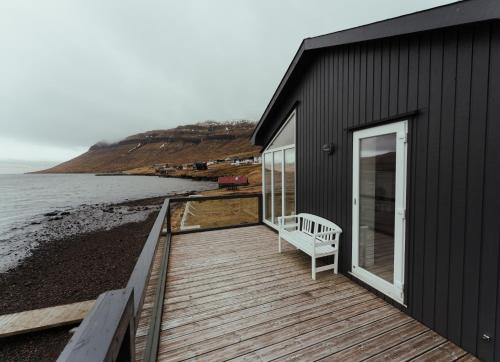 a black house with a wooden deck next to the water at Waterfront retreat - 2 BR Boathouse in Oyrareingir