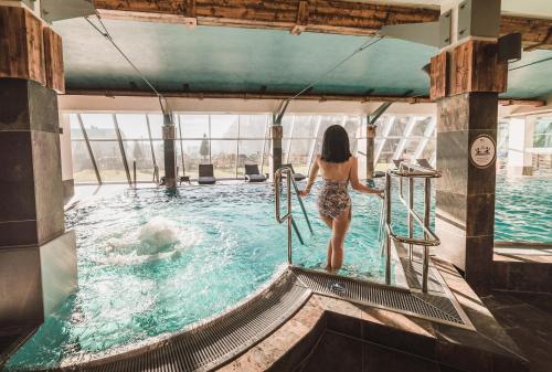 a woman walking into a swimming pool at Młyn Jacka Hotel & Spa in Wadowice