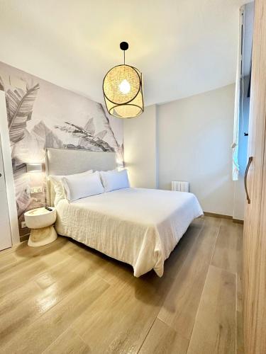 a bedroom with a white bed and a chandelier at Apartamentos Noja Playa in Noja
