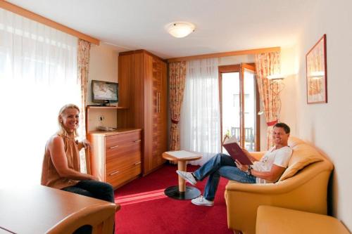 twee mensen zitten in een woonkamer een boek te lezen bij Tirolerhof - Super Sommer Card included in Serfaus