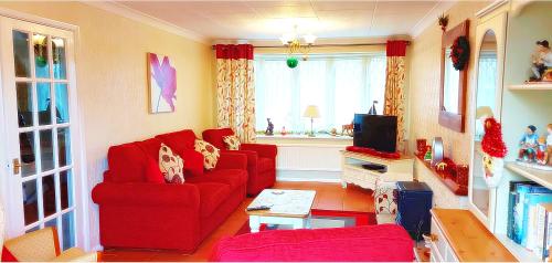 a living room with a red couch and a tv at Sunshine Cottage - You'll adore this Fabulous Holiday Gem Just mins from the Beach for the Perfect Seaside Getaway with FREE Parking & Fast FREE WiFi! 3 Bed & Sleeps 1 to 5 Guests in Chapel Saint Leonards