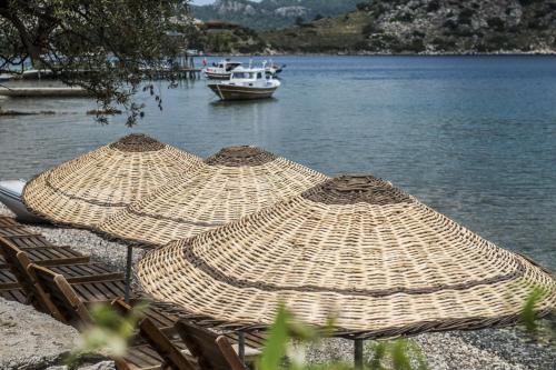 three straw umbrellas on the shore of a lake with a boat at Les Terrasses De Selimiye in Selimiye