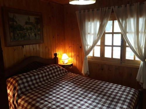 een slaapkamer met een bed met een geruite deken en een raam bij Cabaña Familiar El Refugio in Potrerillos