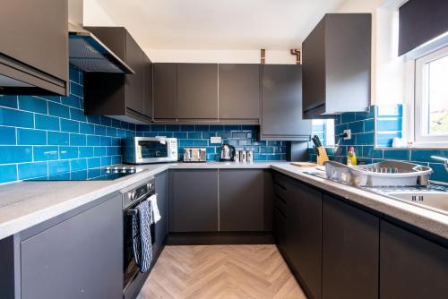 a kitchen with black cabinets and blue tiles at Newly Refurbished Homely 4BR in Sherwood in Nottingham