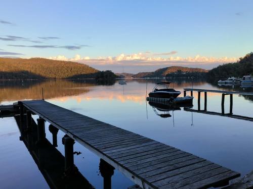 a boat is docked next to a dock on a lake at Cosy Cottage Above the Hawkesbury w/ Jetty in Mooney Mooney