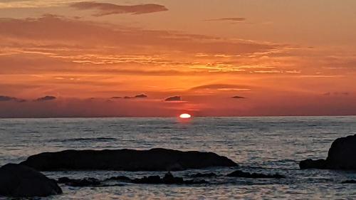 a sunset over the ocean with rocks in the foreground at The Cube Best Vacation Ever in Sìnnai