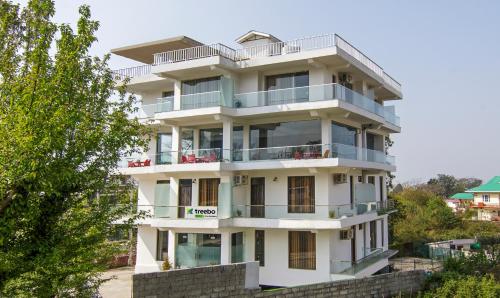 a white building with balconies and trees at Treebo Ortus Residency in Dharamshala