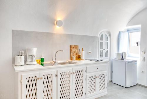 a white kitchen with a sink and a white refrigerator at Aris Caves in Oia