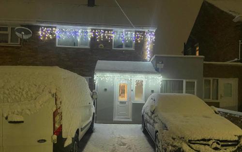 two snowcovered cars parked in front of a house with christmas lights at Peaceful and Novel Place to Stay in Abbey Wood