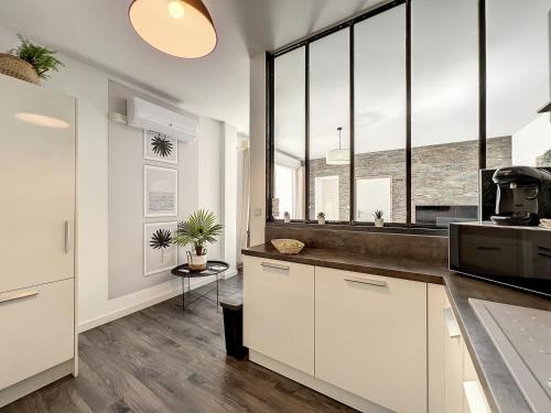 - une cuisine avec des placards blancs et de grandes fenêtres dans l'établissement Appart T3 LE PATIO - avec terrasse, à Boujan-sur-Libron