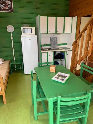 La cuisine est équipée d'une table et de chaises vertes ainsi que d'un réfrigérateur. dans l'établissement Camping municipal de la Lande, à Nexon