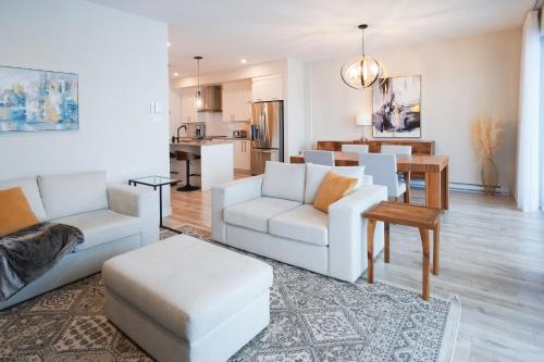 a living room with two white chairs and a table at Le Riverain - Condo neuf au bord de l'eau in Shawinigan