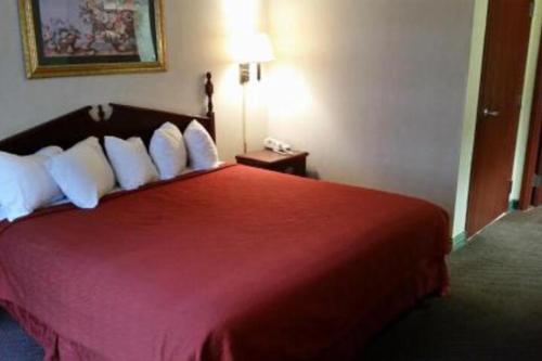 um quarto de hotel com uma cama vermelha com almofadas brancas em ARK SUITES em Jonesboro