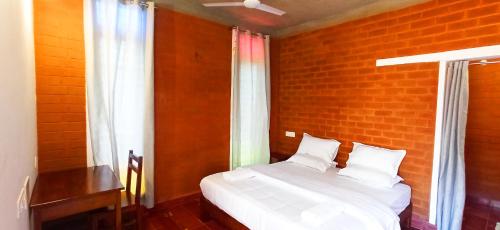 a bedroom with a white bed with a brick wall at Wow Farm House & Resort near Pondicherry in Auroville