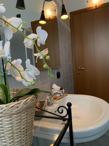 baño con lavabo y cesta con flores blancas en La Corte di Silvia Malpensa, en Cardano al Campo