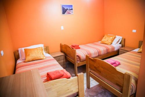 3 camas en una habitación con paredes de color naranja en Hostal Chaxa en San Pedro de Atacama