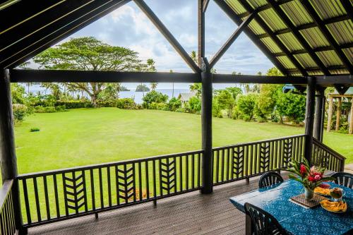 un porche cubierto con mesa, sillas y un campo verde en Raintree Gardens - 1 Acre, Ocean Views, Steps from beach, en Matei