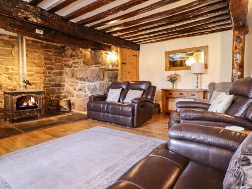 a living room with leather furniture and a stone fireplace at Cwm Yr Afon Mawr in Llanbedr