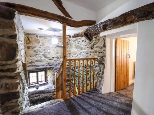 a room with a stone wall and a wooden staircase at Cwm Yr Afon Mawr in Llanbedr