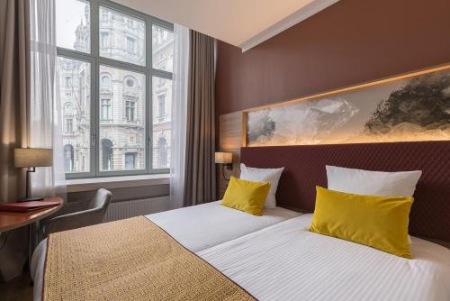 una habitación de hotel con una cama con almohadas amarillas y una ventana en Leonardo Hotel Antwerpen en Amberes