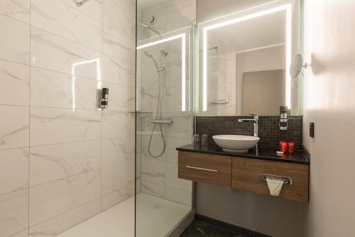 a bathroom with a sink and a shower with a mirror at Leonardo Hotel Antwerpen in Antwerp