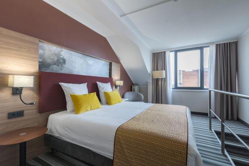 a hotel room with a large bed with yellow pillows at Leonardo Hotel Antwerpen in Antwerp