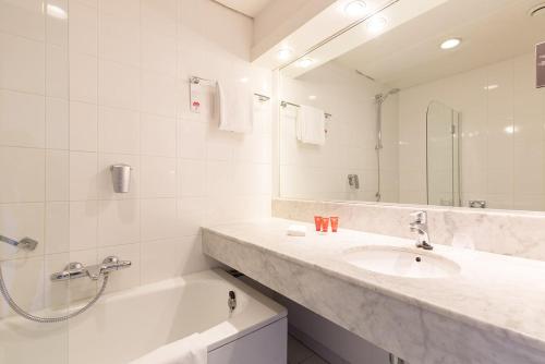 bagno con lavandino, vasca e specchio di Leonardo Hotel Lelystad City Center a Lelystad