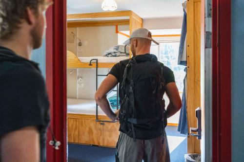 Ein Mann mit einem Rucksack vor einem Etagenbett in der Unterkunft The Flaming Kiwi Backpackers in Queenstown