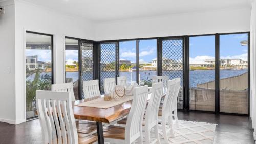 a dining room with a table and white chairs at Opulent Canal-Front Retreat in Banksia Beach