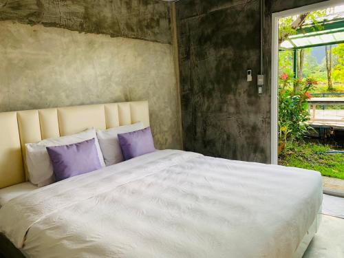 a bedroom with a large white bed with purple pillows at ปานีวิลล์ รีสอร์ต in Ban Wang Takhrai