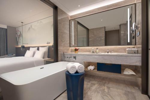 um quarto de hotel com uma banheira, uma cama e um espelho em Pullman Huai'an 淮安铂尔曼酒店 em Huai'an