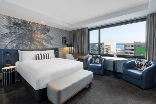 Habitación de hotel con cama, sillas y ventana grande. en Imagine Beach Road, en Auckland