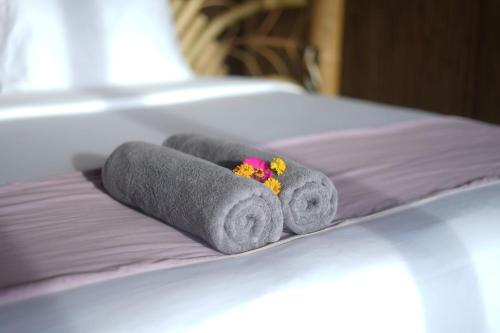 2 toallas enrolladas con flores en una cama en Kini Resort - Oceanfront Bamboo Eco Lodges, en Sekongkang