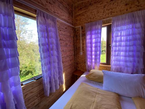 a bedroom with a bed and a window with purple curtains at La Padurea Mica in Cărbunari