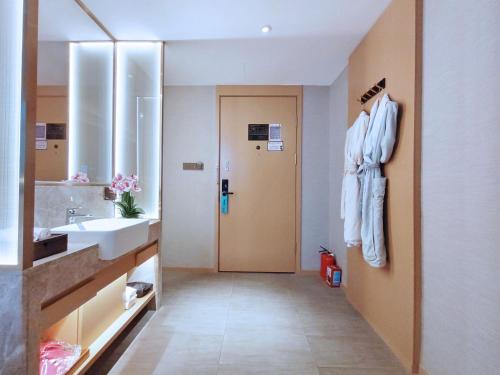 a bathroom with a sink and a mirror and a robe at Paco Hotel Guangzhou South Railway Station Panyu Changlong Branch in Guangzhou